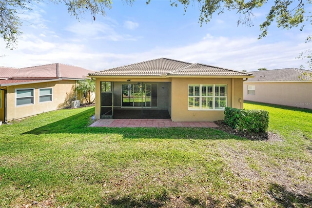 back of house featuring stucco siding, a lawn, a tile roof, a patio, and a sunroom