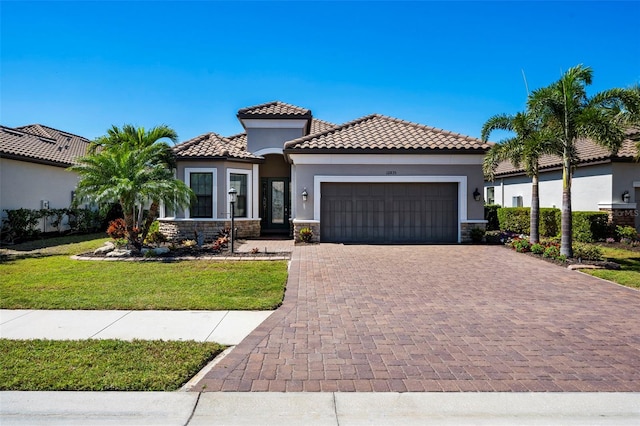 mediterranean / spanish house with a front lawn, a garage, stone siding, a tile roof, and decorative driveway