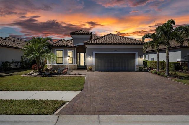 mediterranean / spanish home featuring stone siding, a garage, decorative driveway, and stucco siding