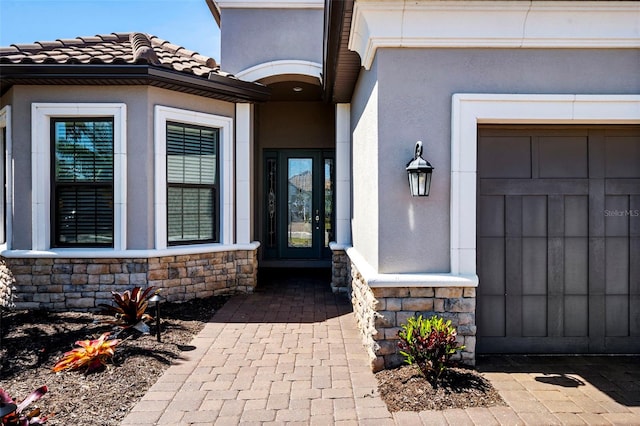 view of exterior entry with stucco siding, stone siding, a garage, and a tiled roof