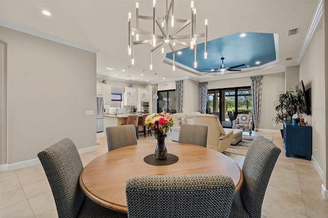 dining room with crown molding, baseboards, a tray ceiling, ceiling fan with notable chandelier, and light tile patterned flooring