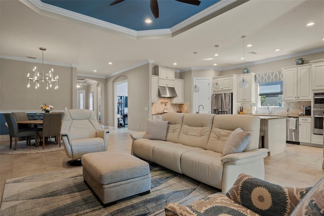 living area with a tray ceiling, ornamental molding, light tile patterned floors, recessed lighting, and ceiling fan with notable chandelier