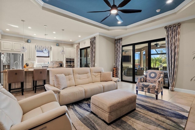 living area with baseboards, light tile patterned flooring, ornamental molding, ceiling fan, and a raised ceiling