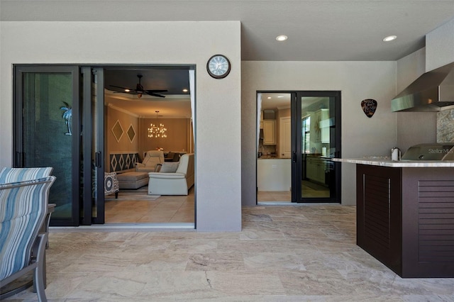 kitchen featuring recessed lighting, ceiling fan with notable chandelier, and wall chimney range hood