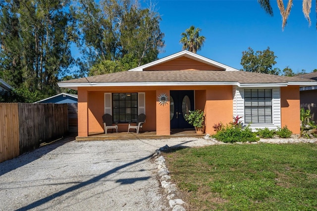 view of front of house featuring covered porch, stucco siding, a front lawn, and fence