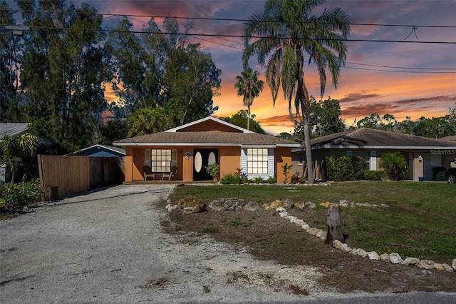 view of front facade featuring stucco siding, gravel driveway, a front lawn, and fence