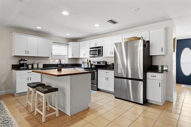 kitchen featuring visible vents, a center island, appliances with stainless steel finishes, white cabinets, and butcher block counters