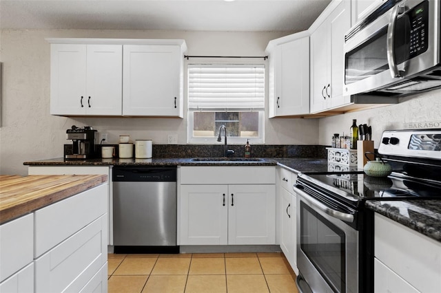 kitchen featuring dark stone counters, light tile patterned floors, appliances with stainless steel finishes, white cabinets, and a sink