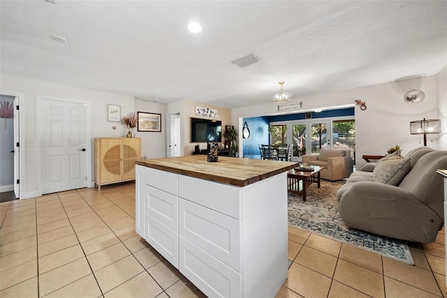 kitchen featuring butcher block countertops, open floor plan, light tile patterned flooring, and white cabinets