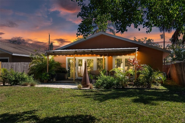 back of house at dusk featuring a patio area, fence, and a lawn