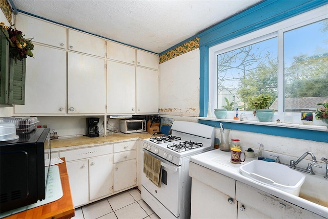 kitchen with black microwave, light tile patterned floors, a sink, light countertops, and white gas range oven