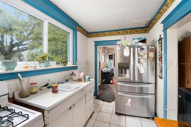 kitchen featuring gas range oven, white cabinetry, light tile patterned flooring, a sink, and stainless steel fridge