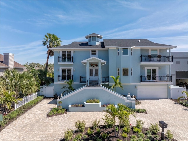 view of front of house with a fenced front yard, decorative driveway, french doors, an attached garage, and a balcony