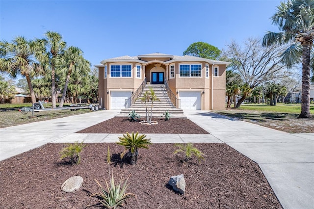 view of front of home with stairs, driveway, an attached garage, and stucco siding