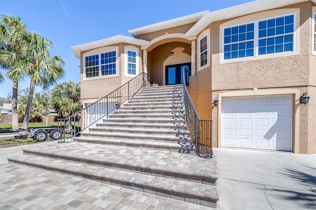 view of front of home featuring a garage, french doors, stairway, and stucco siding