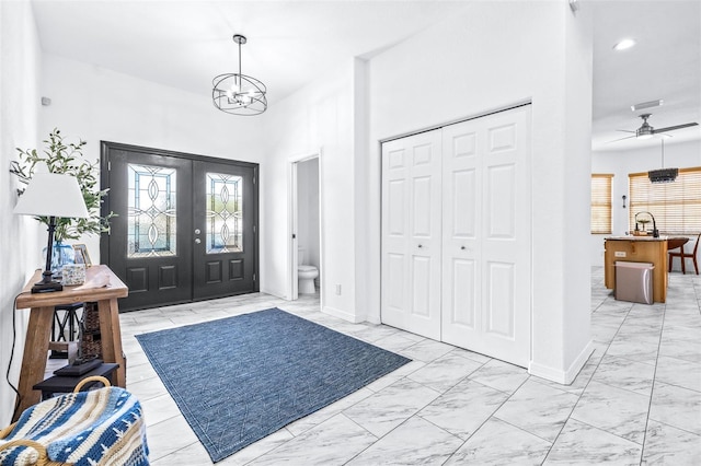 foyer entrance with ceiling fan with notable chandelier, visible vents, baseboards, marble finish floor, and french doors