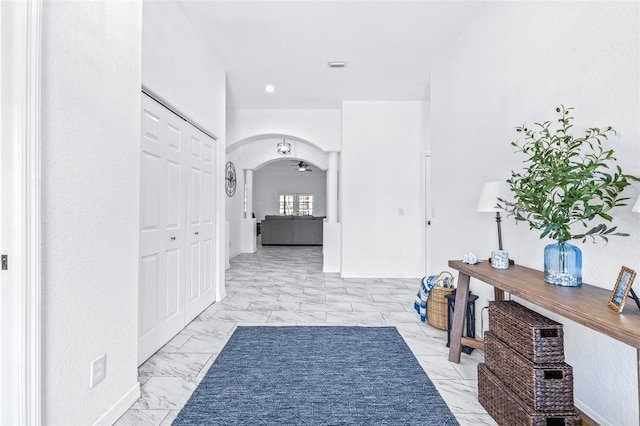 hallway featuring marble finish floor, baseboards, arched walkways, and recessed lighting