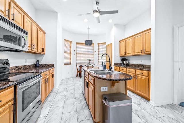 kitchen with a kitchen island with sink, a sink, marble finish floor, appliances with stainless steel finishes, and dark stone counters