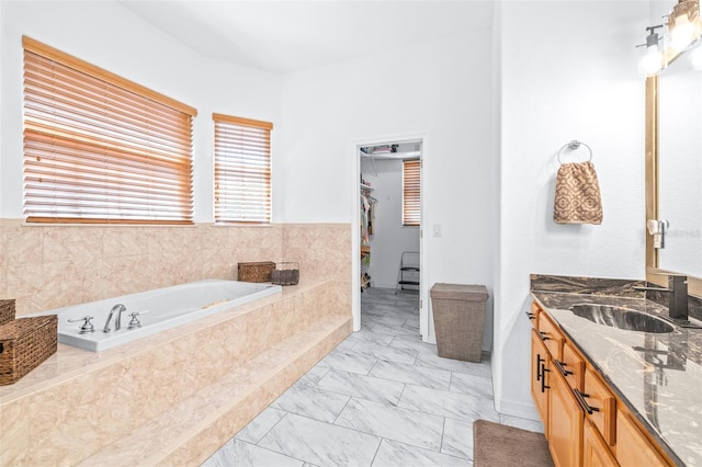 bathroom with a walk in closet, marble finish floor, a garden tub, and vanity