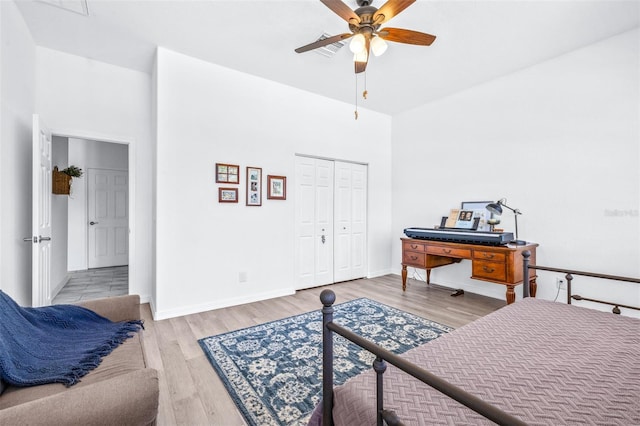 bedroom with a towering ceiling, a ceiling fan, baseboards, a closet, and light wood-type flooring