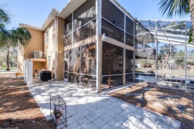 view of home's exterior featuring a patio, central AC, glass enclosure, and stucco siding