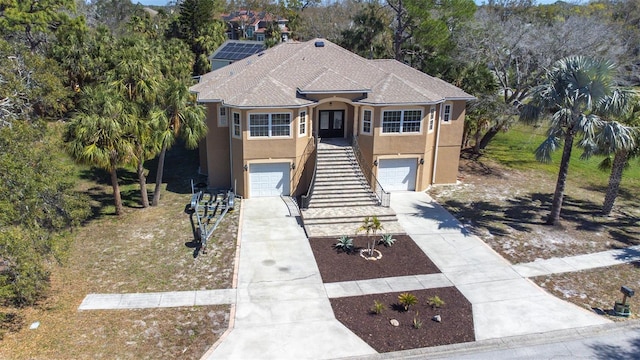 coastal inspired home featuring a garage, stairs, driveway, and stucco siding