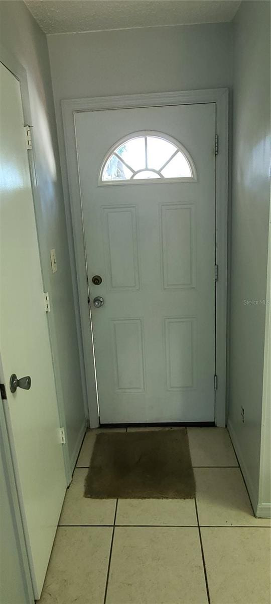 doorway to outside with light tile patterned flooring and a textured ceiling