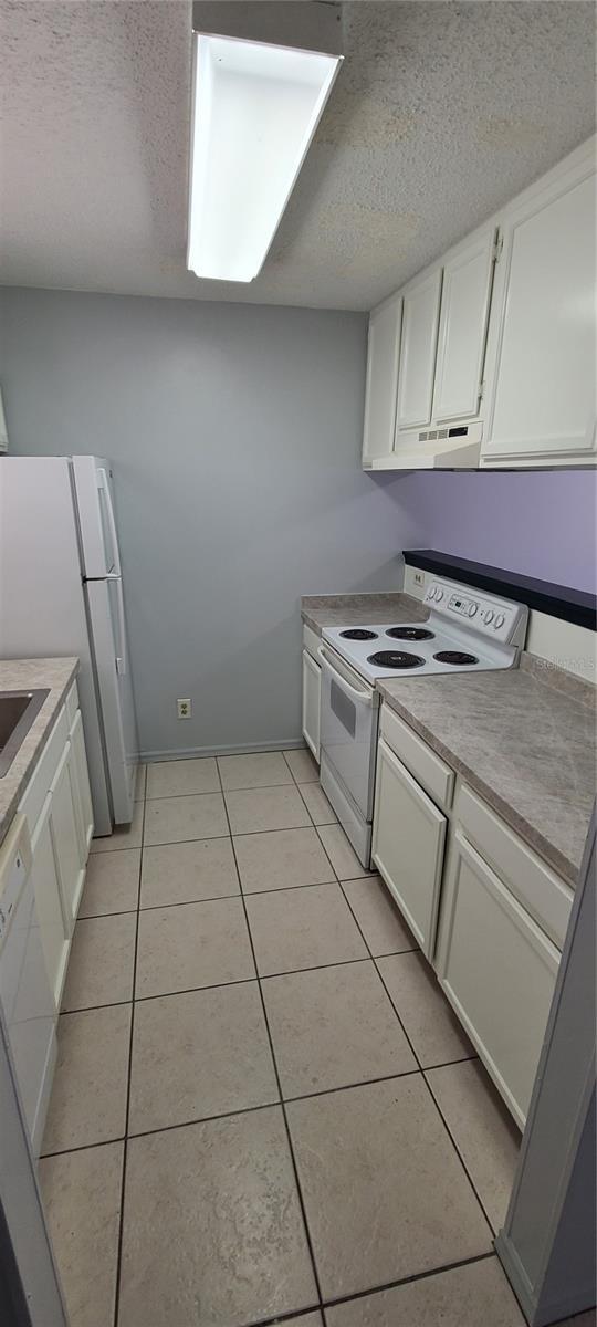 kitchen with white cabinets, white appliances, under cabinet range hood, and light tile patterned floors