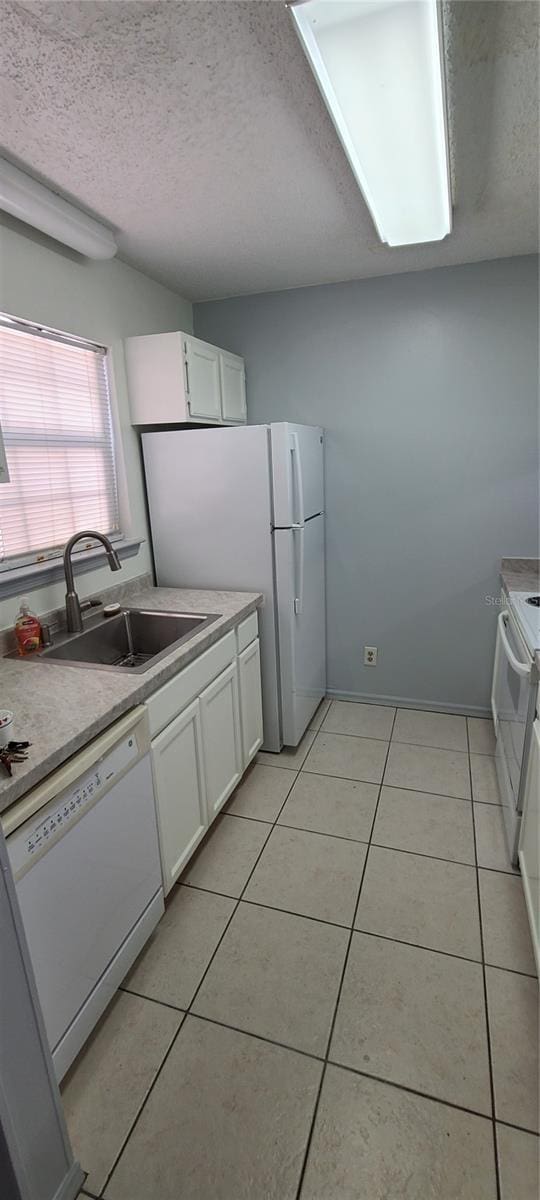 kitchen with white appliances, light tile patterned floors, white cabinets, a textured ceiling, and a sink