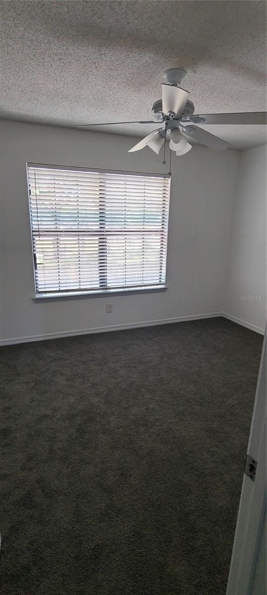 unfurnished room with a textured ceiling, dark carpet, baseboards, and a healthy amount of sunlight