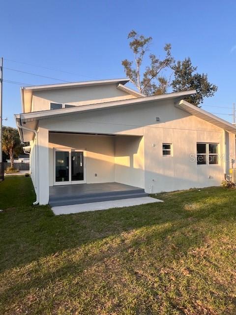 back of house with a lawn, a patio area, and stucco siding