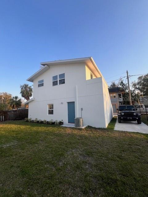 back of house featuring central AC, a lawn, and stucco siding