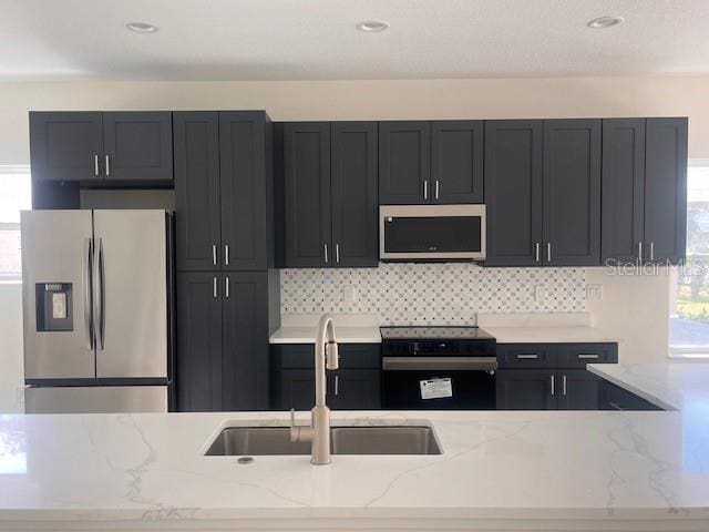 kitchen featuring light stone countertops, tasteful backsplash, appliances with stainless steel finishes, and a sink