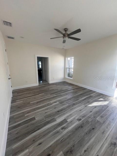 spare room with dark wood-style flooring, visible vents, and baseboards