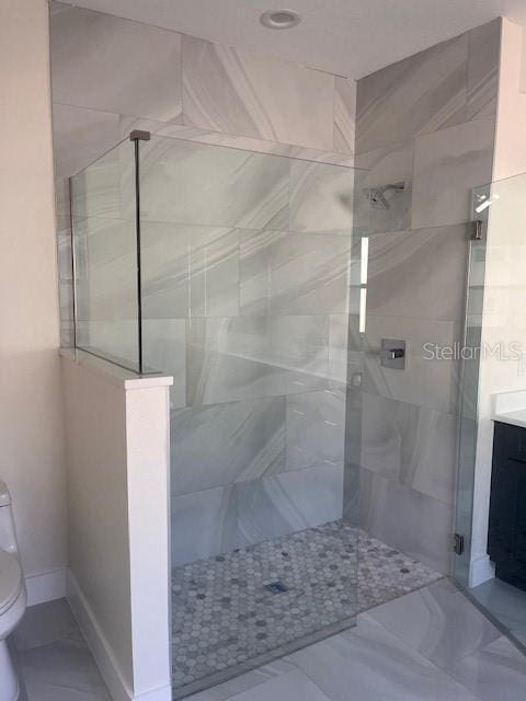 full bathroom with baseboards, tiled shower, vanity, and toilet