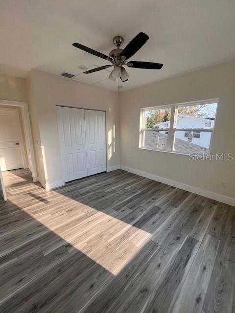 unfurnished bedroom featuring ceiling fan, wood finished floors, visible vents, baseboards, and a closet