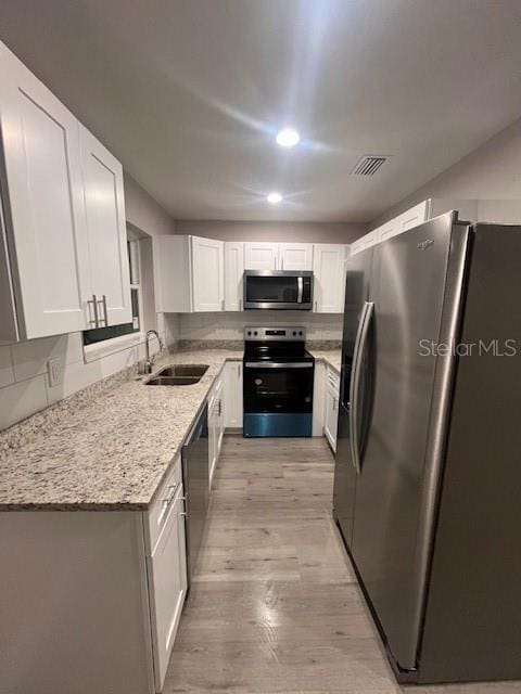 kitchen featuring light stone counters, stainless steel appliances, a sink, light wood-style floors, and white cabinets