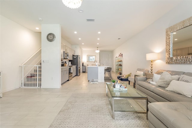 living area featuring light tile patterned floors, visible vents, stairs, a notable chandelier, and recessed lighting