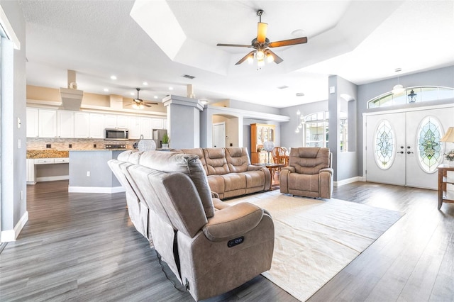 living area with a ceiling fan, a raised ceiling, visible vents, and wood finished floors