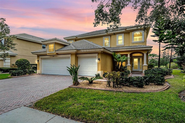 view of front of house featuring decorative driveway, a yard, an attached garage, and stucco siding