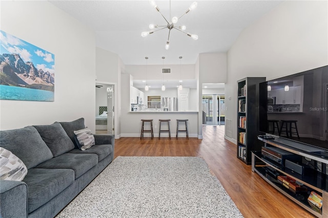 living room with visible vents, an inviting chandelier, wood finished floors, high vaulted ceiling, and baseboards