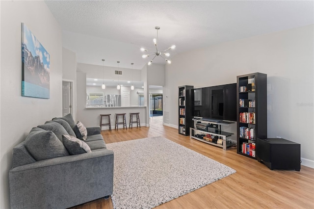 living area with light wood finished floors, visible vents, an inviting chandelier, a textured ceiling, and baseboards