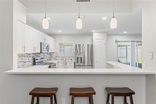 kitchen featuring tasteful backsplash, light countertops, hanging light fixtures, appliances with stainless steel finishes, and a peninsula