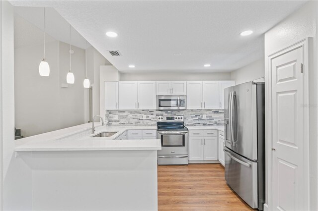 kitchen with visible vents, appliances with stainless steel finishes, a peninsula, white cabinetry, and a sink