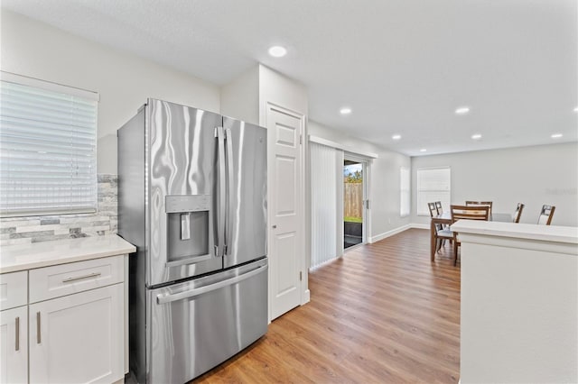 kitchen with stainless steel fridge, light countertops, light wood-type flooring, white cabinetry, and recessed lighting