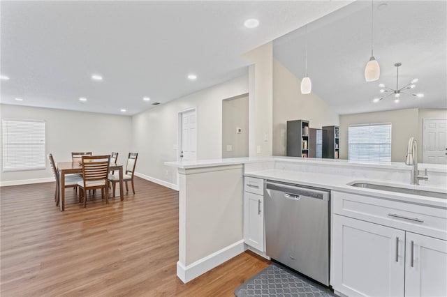 kitchen featuring light wood-style flooring, hanging light fixtures, light countertops, stainless steel dishwasher, and a sink