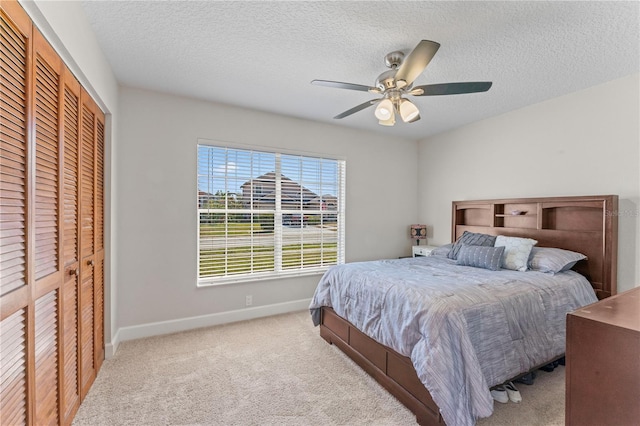 carpeted bedroom with a closet, a textured ceiling, baseboards, and a ceiling fan