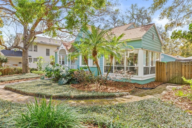 view of front facade with a sunroom, roof with shingles, and fence