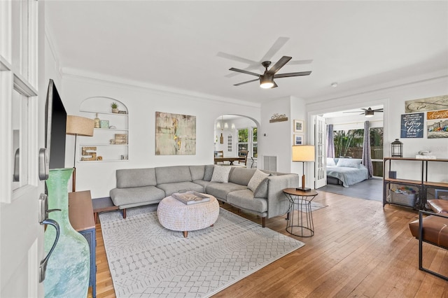 living area featuring arched walkways, ceiling fan, hardwood / wood-style flooring, visible vents, and ornamental molding