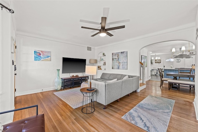 living room featuring arched walkways, wood-type flooring, ornamental molding, baseboards, and ceiling fan with notable chandelier